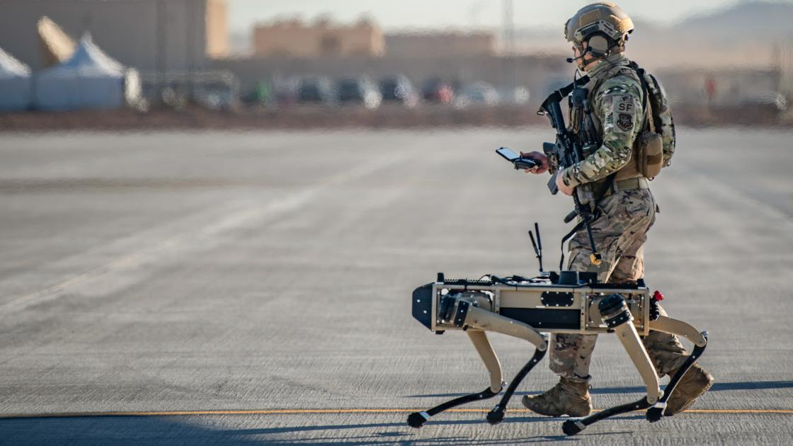 A soldier walking alongside a four-legged military robot.